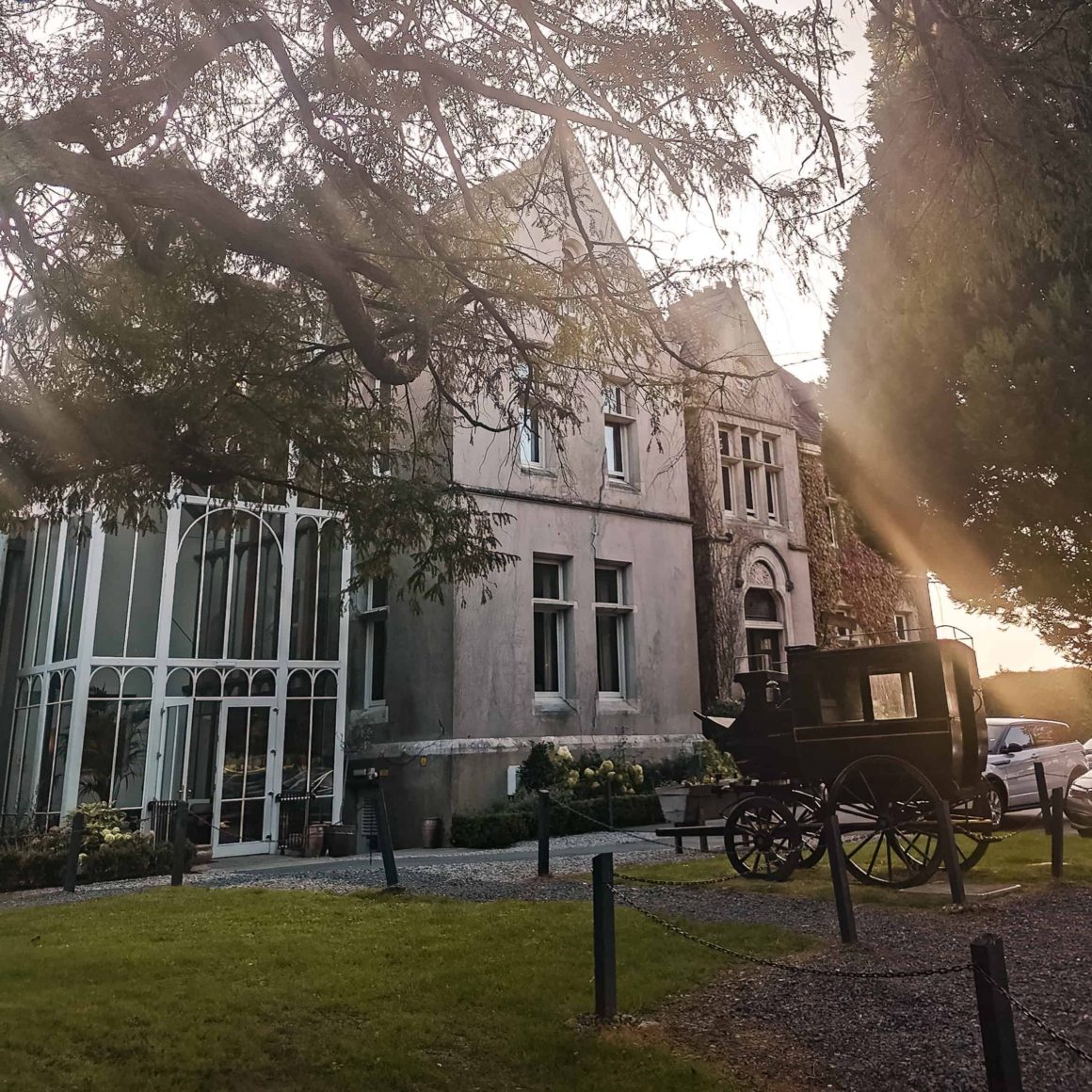 Evening view of Cahernane House Hotel with its historic faรงade, conservatory and traditional horse-drawn carriage in the gardens.