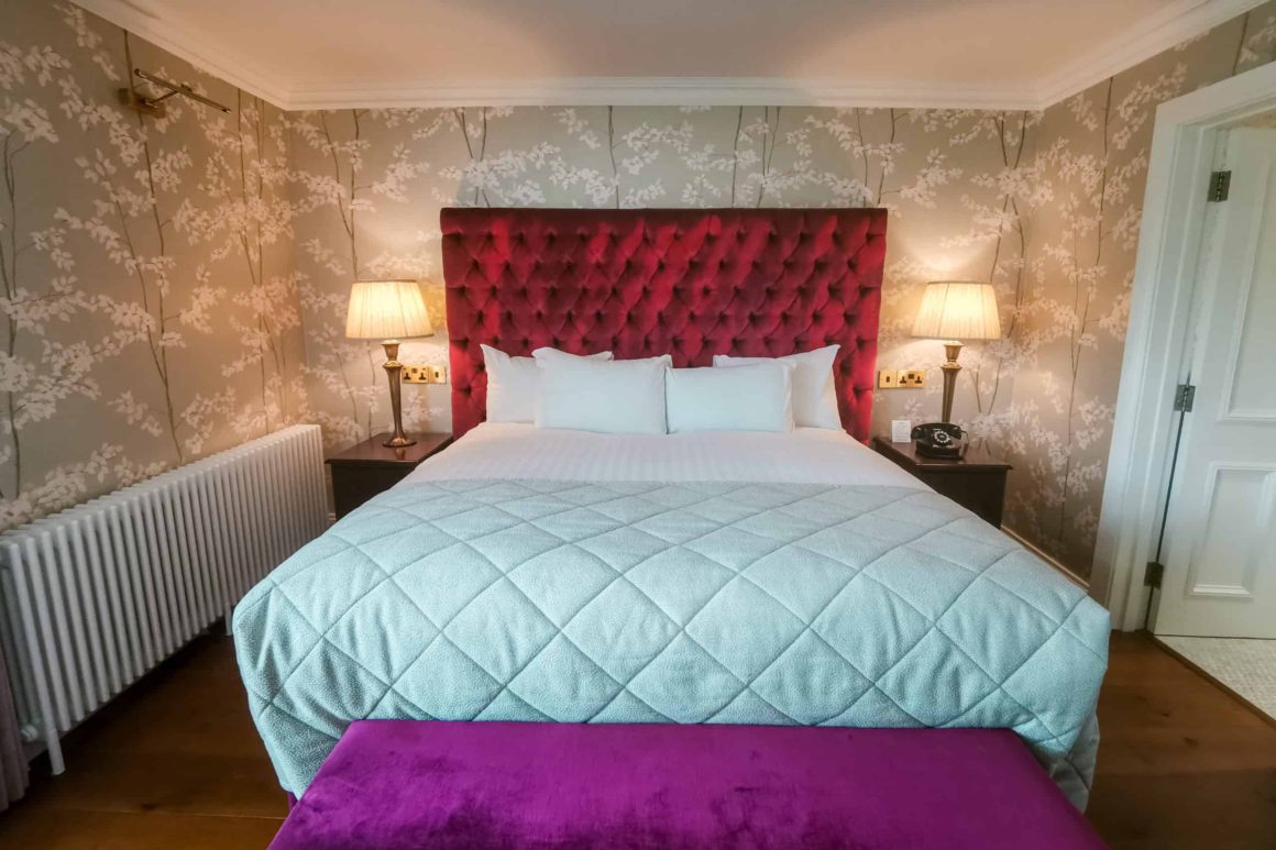 Spacious king bedroom with a striking velvet headboard, elegant wallpaper and luxury bedding at Cahernane House Hotel.