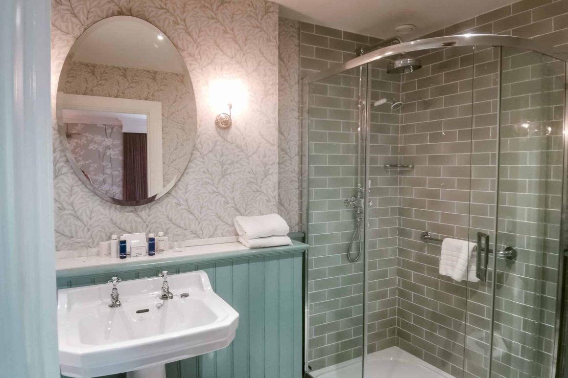The superior double room's bathroom with its shower and tub, white sink, oval mirror, and a small warm lamp