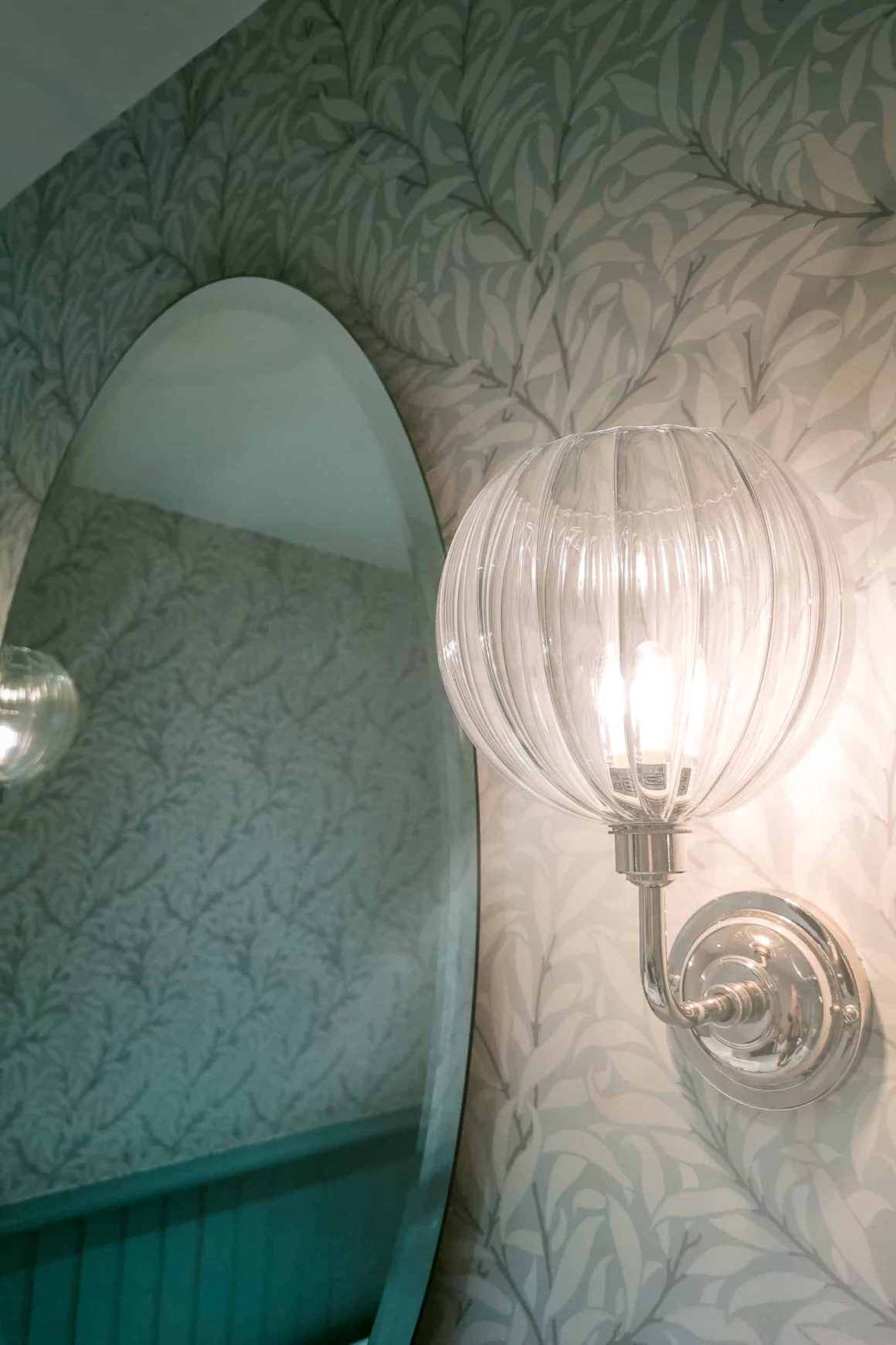Decorative wall light and oval mirror adding classic style to a beautifully designed hotel bathroom.