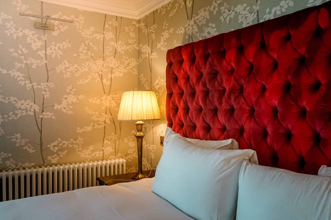 Close-up of a luxurious bed with a deep red velvet headboard and elegant dรฉcor at Cahernane House Hotel.
