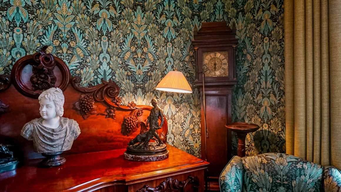 Traditional sitting room featuring antique furniture, ornate wallpaper, a grandfather clock and warm lighting in a historic Irish manor.