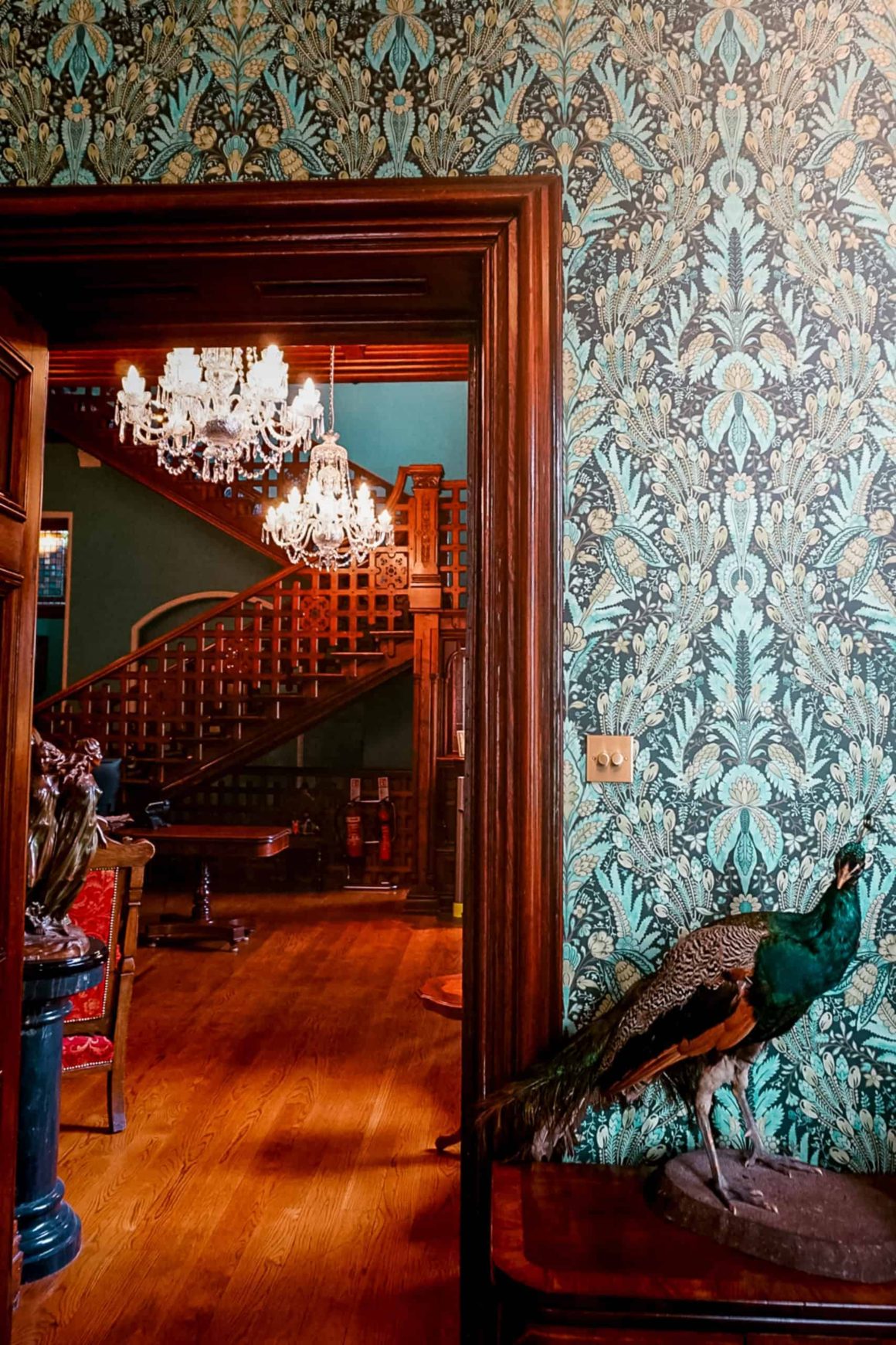 View through an elegant doorway towards a sweeping staircase, crystal chandeliers and period dรฉcor inside a historic Irish country house.