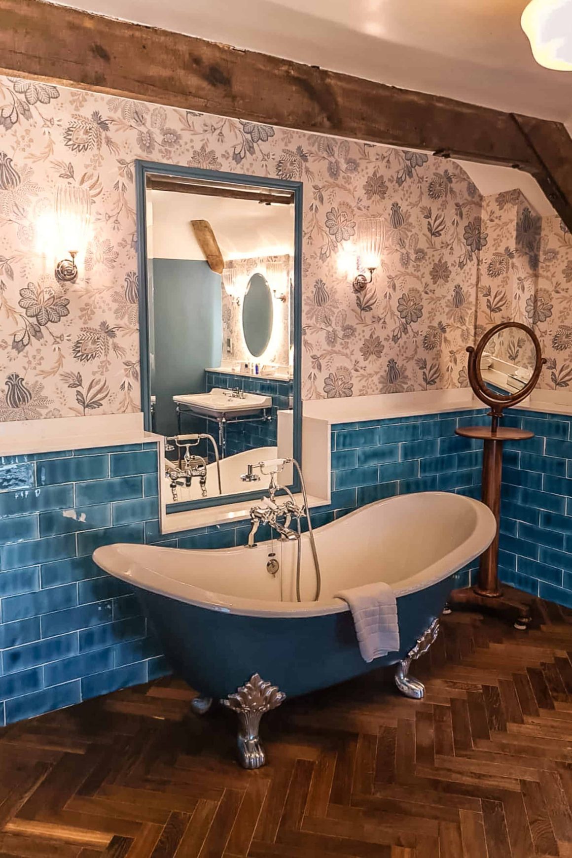 Elegant bathroom featuring a freestanding roll-top bath, blue tiles and floral wallpaper in a luxury suite.