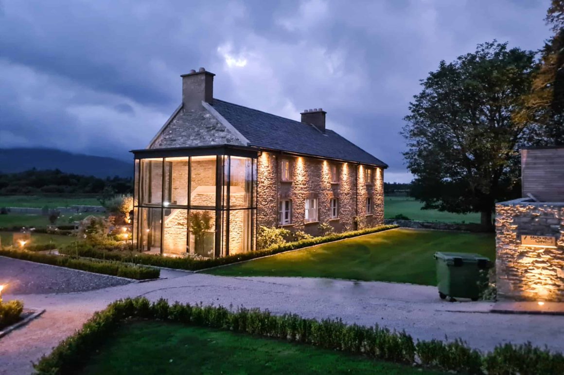Beautifully restored stone lodge illuminated at dusk within the peaceful grounds of a luxury country estate near Killarney.