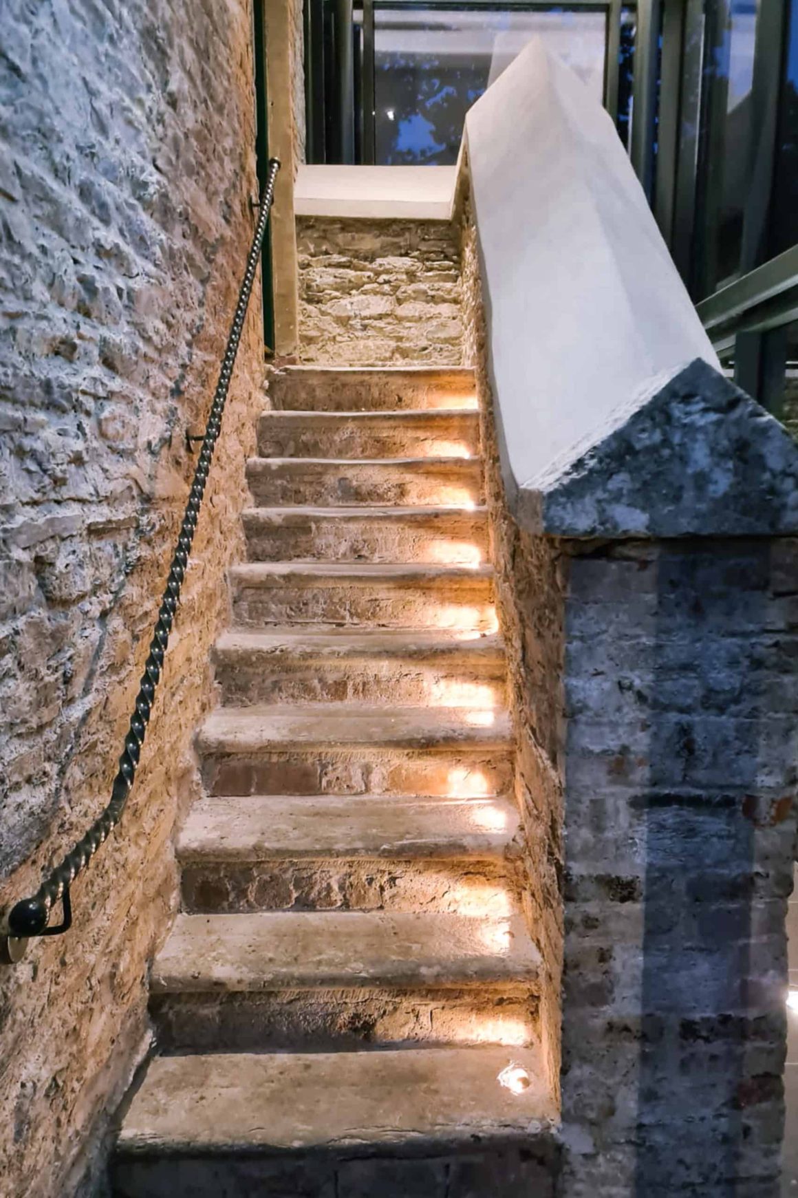 Illuminated stone staircase with exposed walls showcasing the restored historic character of the hotel building.