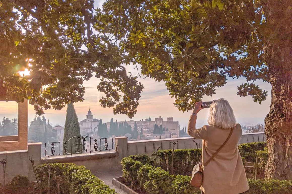 Woman takes picture of sunset through the trees at the Alhambra in Granada, Spain