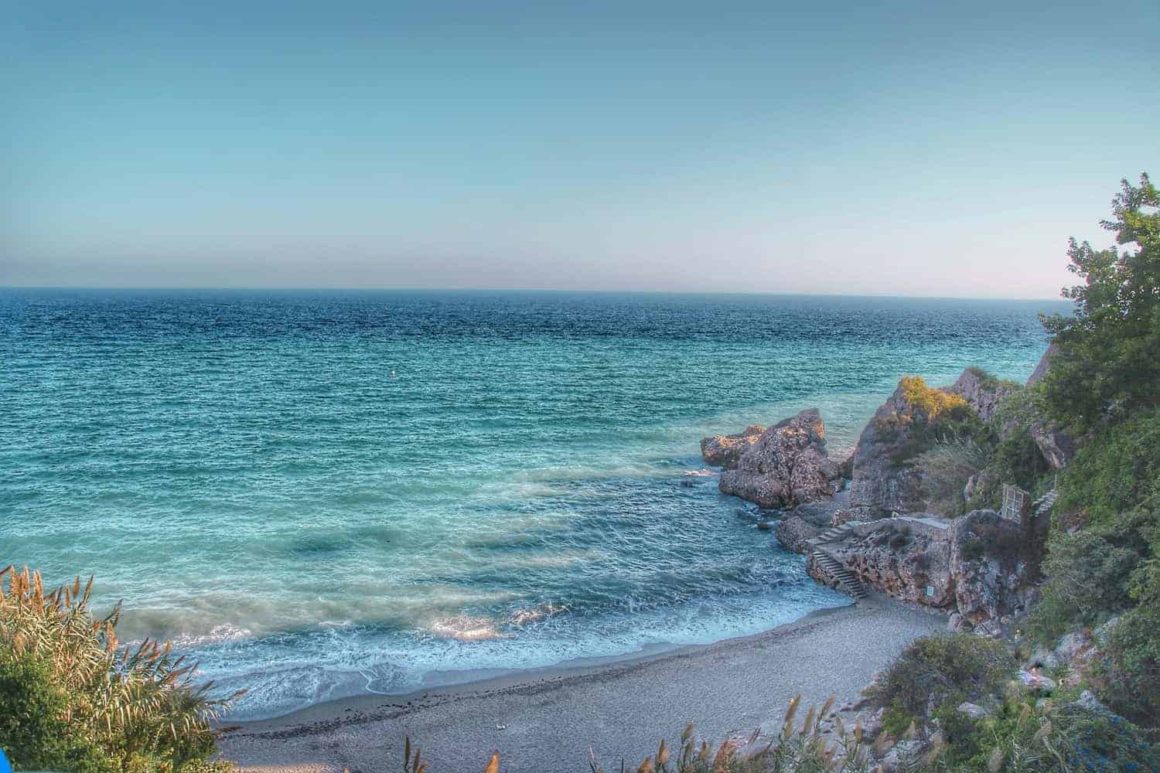 Small secluded beach with clear turquoise Mediterranean water, rocky cliffs and a stone stairway near Nerja, Spain.
