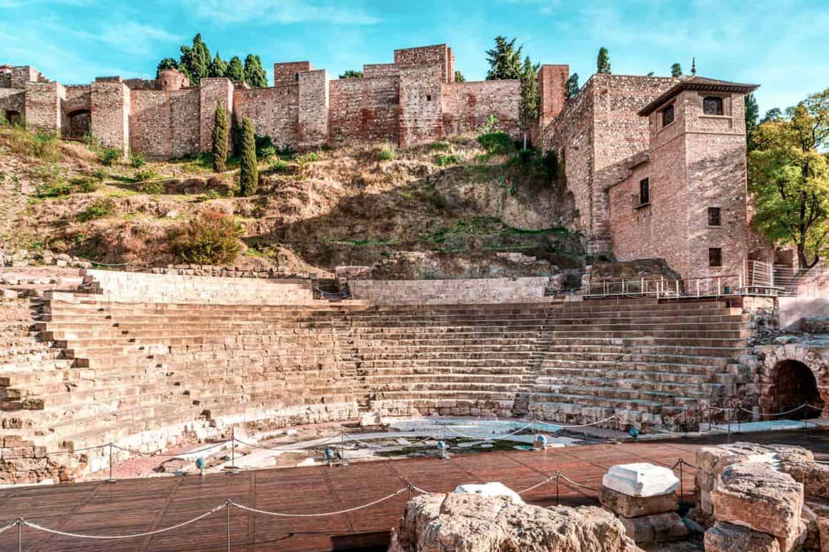 Ancient Roman Theatre in Mรกlaga with stone seating and the fortified walls of the Alcazaba rising behind.