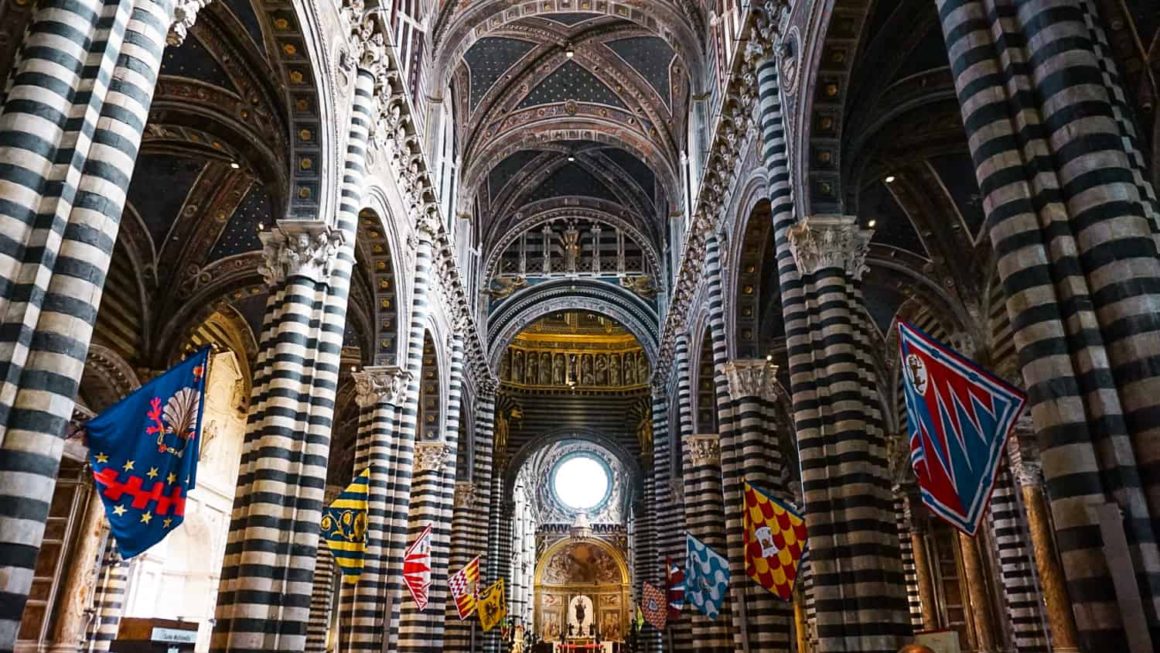 Grand interior of Siena Cathedral with striped marble columns and colourful medieval banners