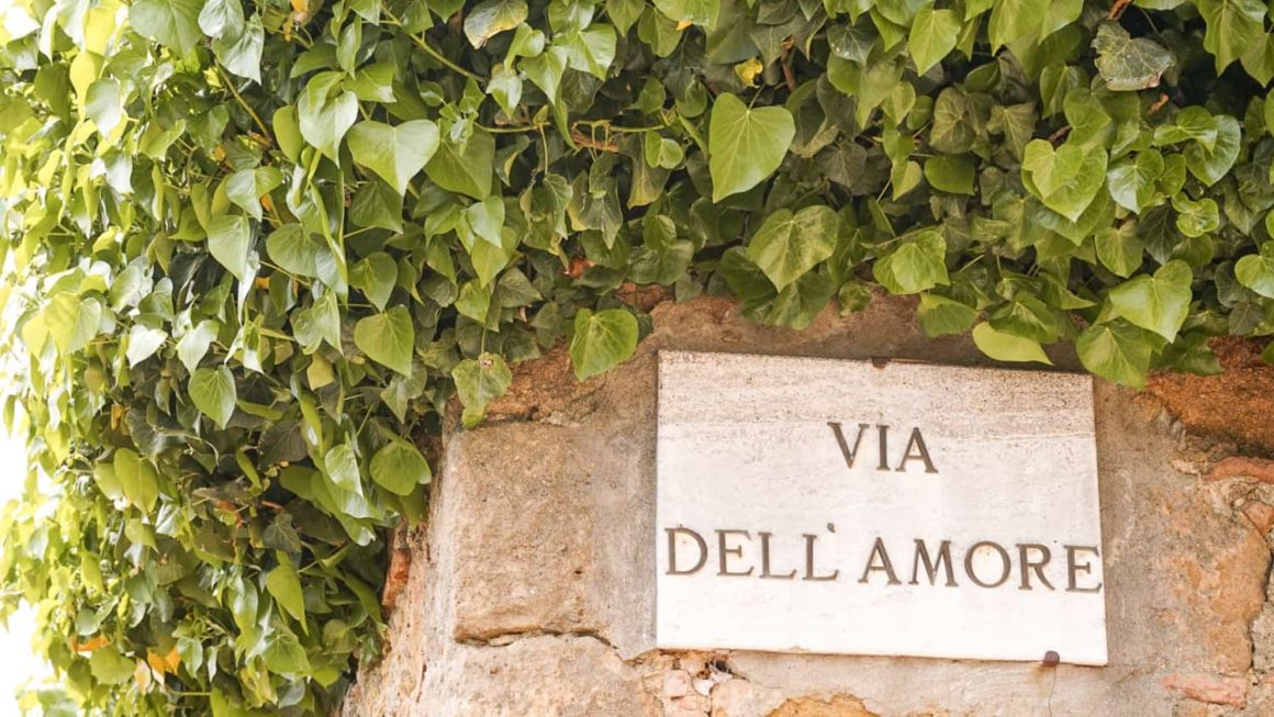 Via dell'Amore street sign surrounded by ivy-covered stone walls in Pienza