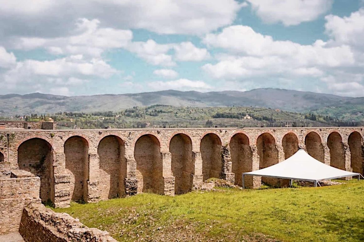 Historic stone arches of a medieval fortress with rolling Tuscan hills in the background