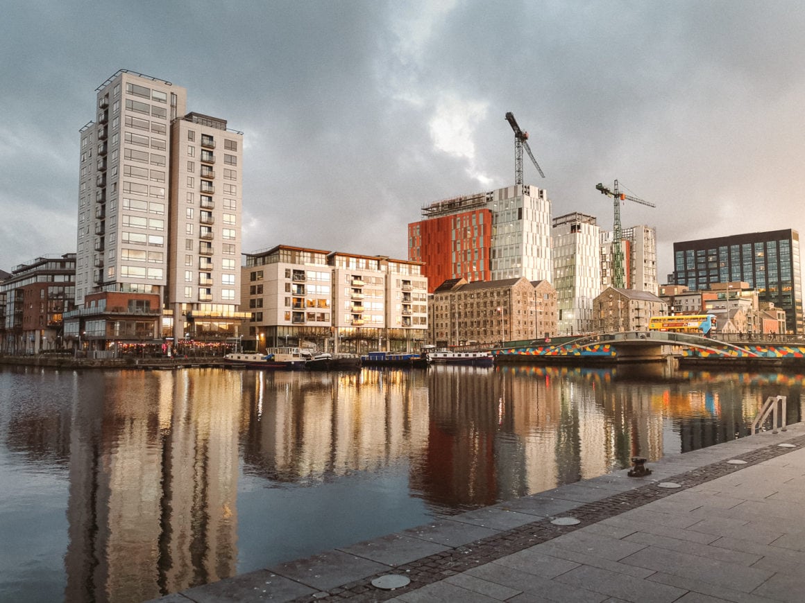 Modern buildings and a colourful bridge reflected in the River Liffey beneath dramatic clouds in Dublin Docklands.
