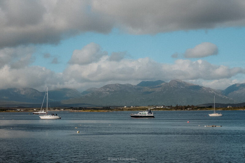 Boats on calm blue water beneath the rugged mountains of Connemara