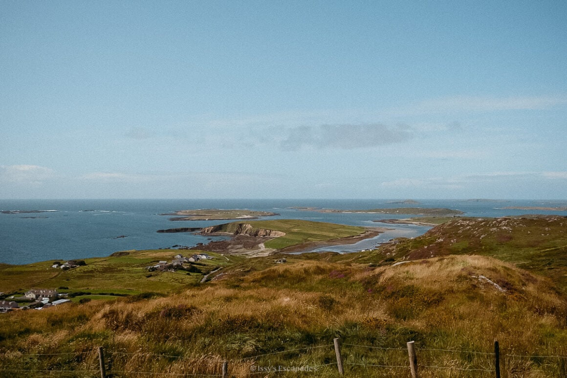 An elevated panorama of fields, scattered houses, islands and ocean beneath a hazy blue sky