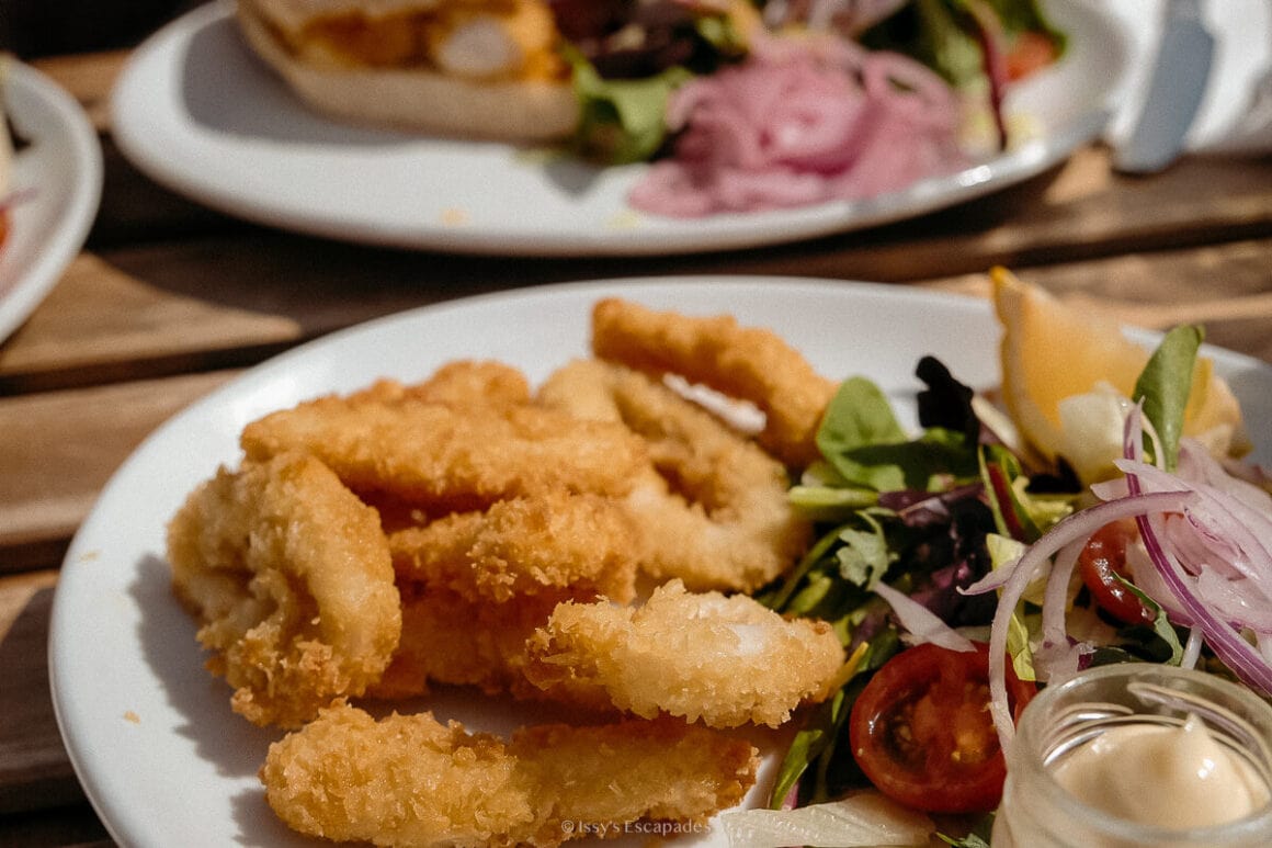 Breaded fried seafood with salad, red onion, lemon and a small pot of dip on a white plate