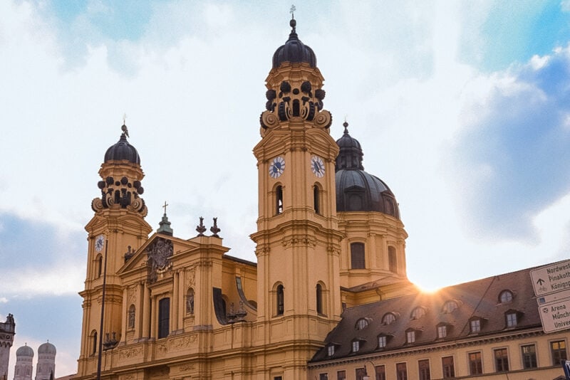 The golden façade and twin towers of the Theatinerkirche in Munich, with sunlight appearing beside the church