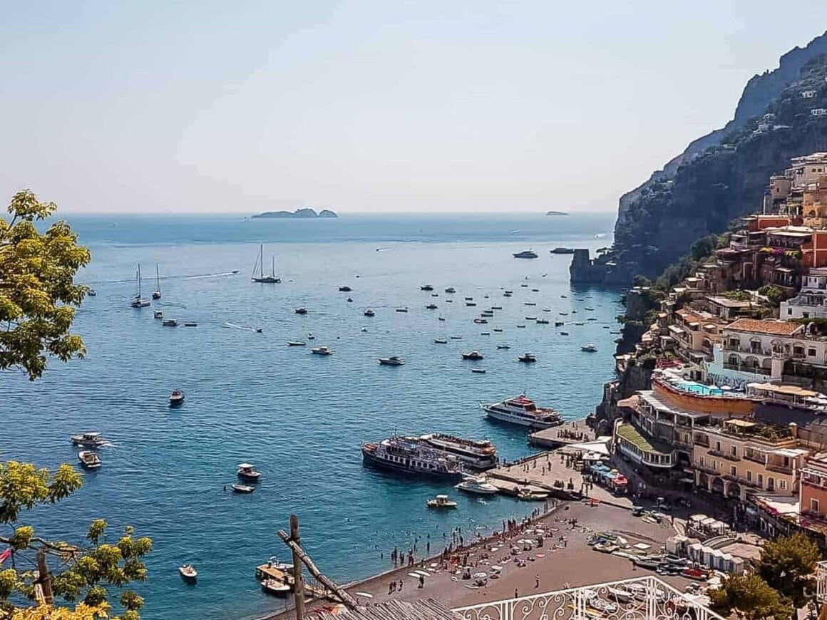 Elevated view over Positano on the Amalfi Coast, with hillside buildings, a beach and boats scattered across the blue Mediterranean Sea.