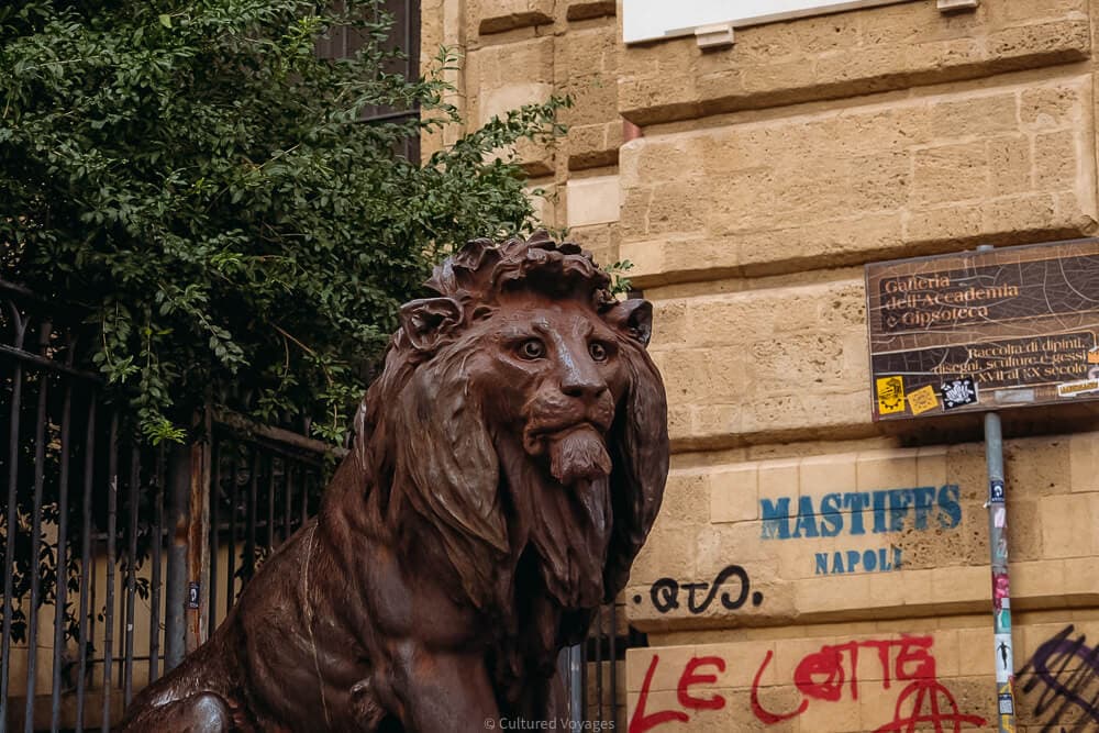 sculpture of lion outside baroque building with graffiti in naples