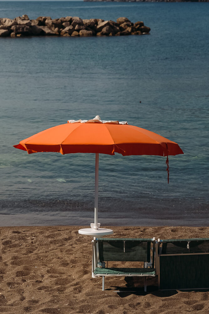 sun umbrella on beach providing shade to a sun lounger on the sand with the clear blue waters in front
