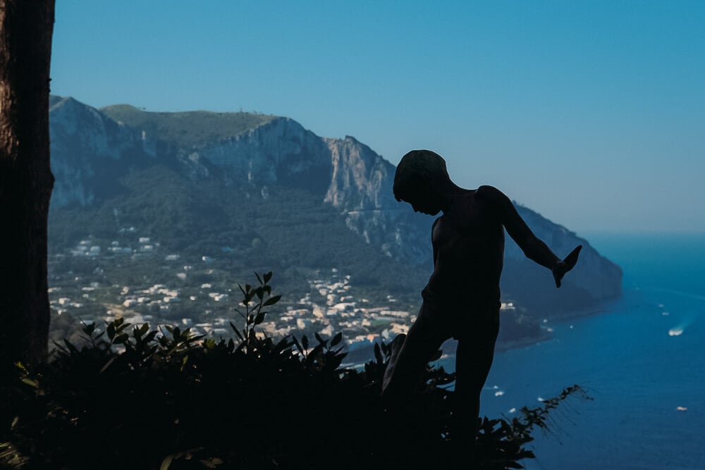 statue of boy in shadow looking over port of capri from a great height