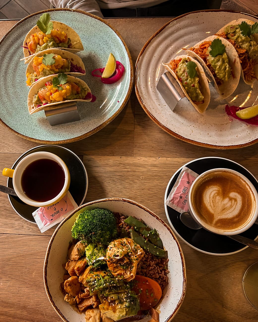 Plates of tacos, a rice bowl meal, and cups of coffee on top of a wooden table in Nicolau Porto