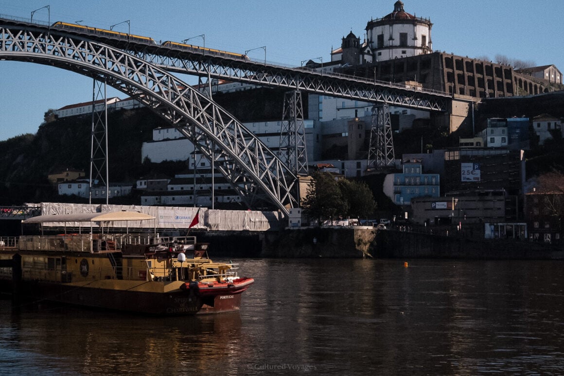 a boat floating on Douro River next to a bridge with houses and buildings lined up in the background