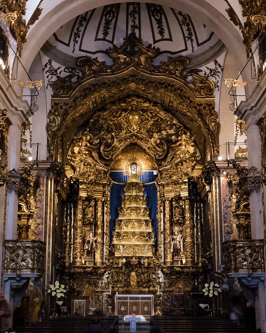 a large golden altar in Igreja do Carmo with intricate carvings, statues, and blue curtains