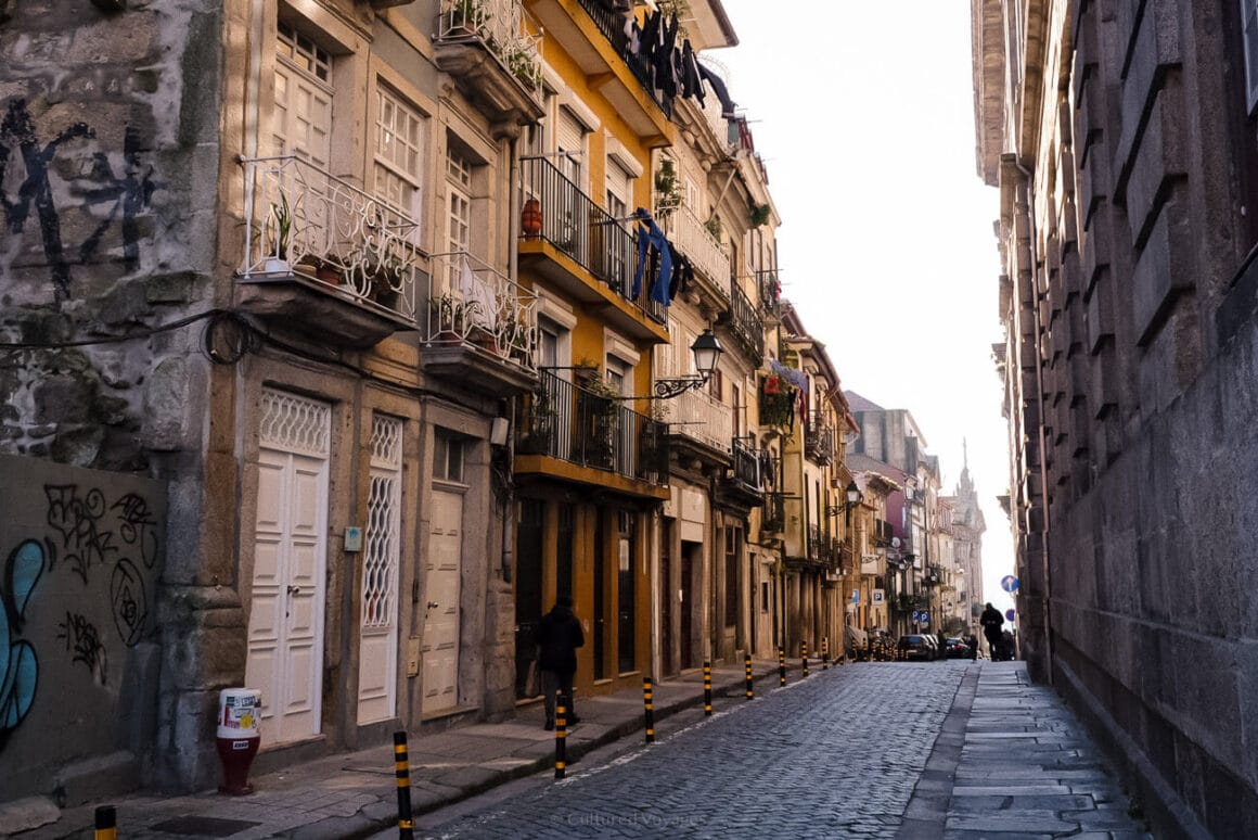 A cobbled road with people walking and facades of houses in warm colors on both sides