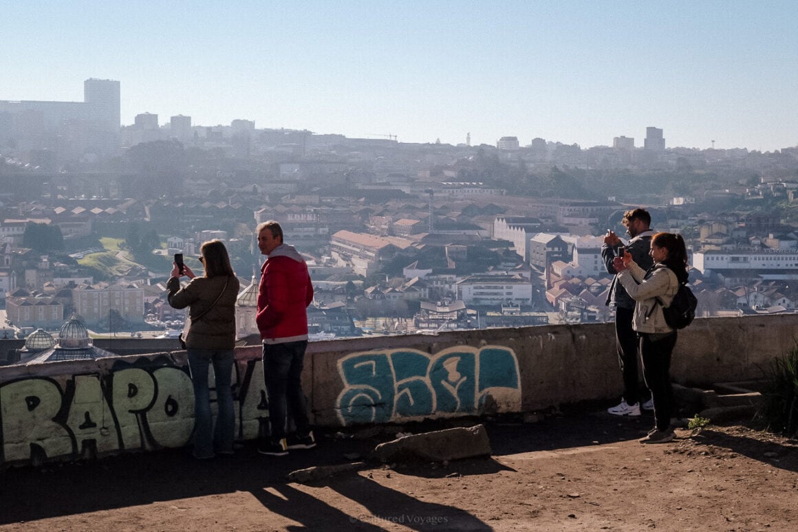 a group of people standing on top of a cement wall taking a photo of the buildings in the background - 1 day in porto itinerary