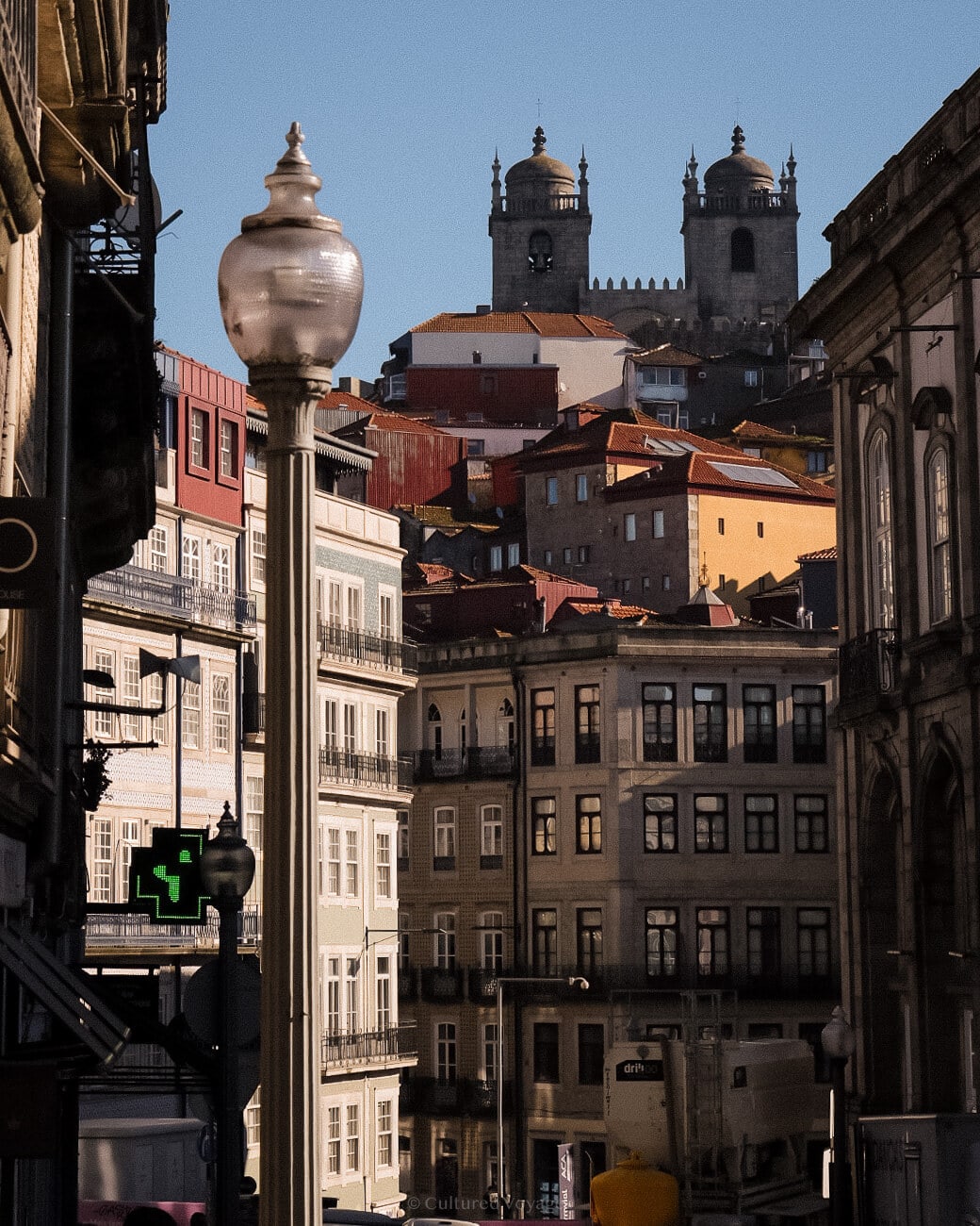 a street lamp in the foreground with the view of buildings in warm colors