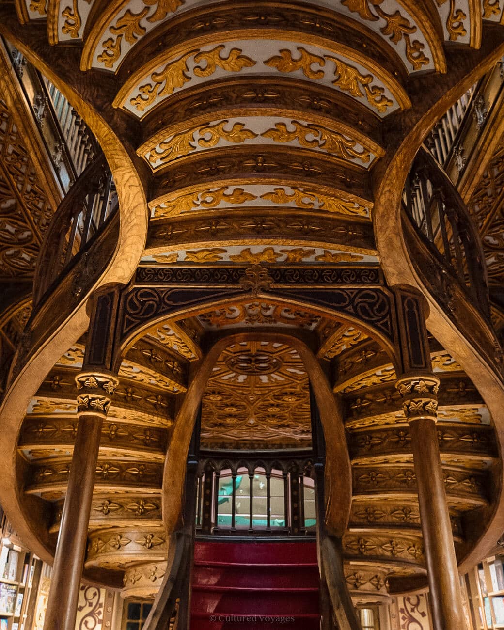 a wooden staircase with intricately carved details and vibrant red steps at Livraria Lello bookstore