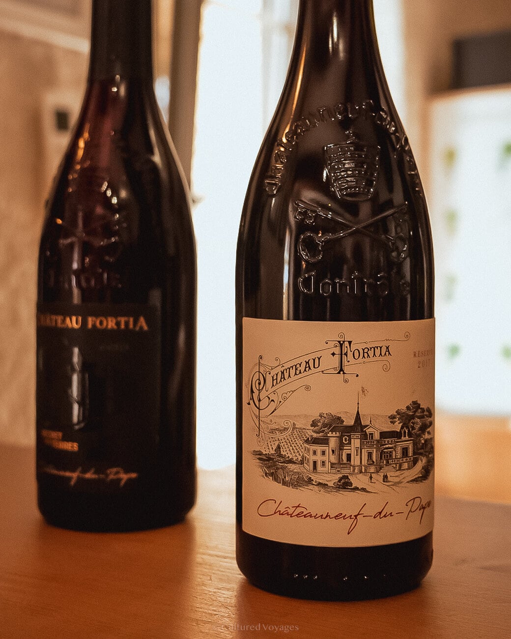 Two wine bottles on a wooden table with one in a white table in the front and the other in a black label in the back