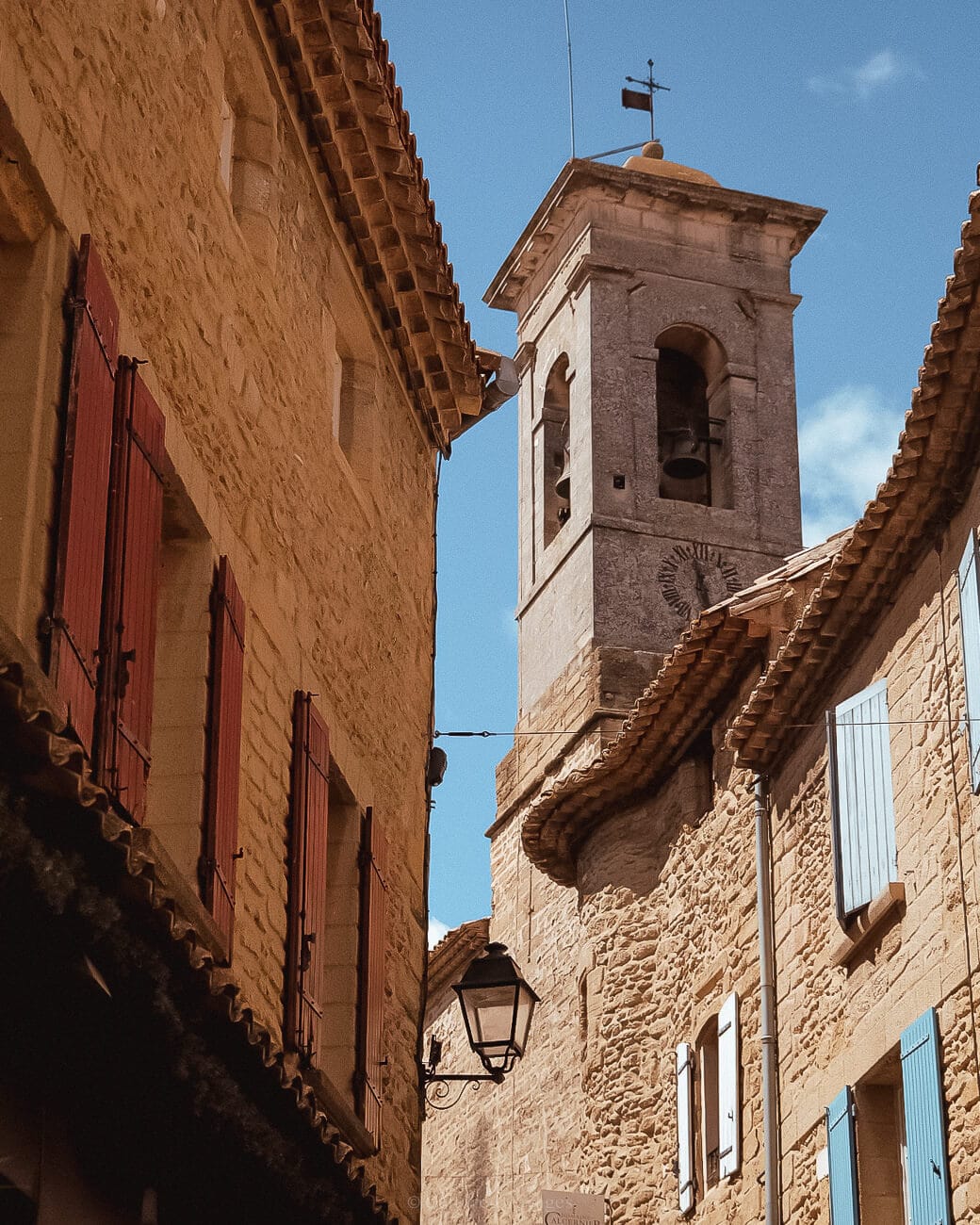 View of a second floor of a stone bricked wall building with windows and a church tower in the background with clock and clear blue skies