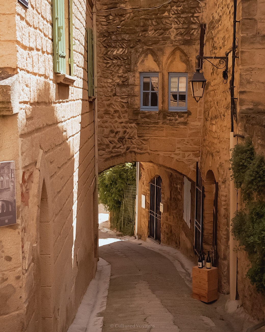A paved street leading surrounded by a stone bricked wall leading into an arched entry way with blue windows