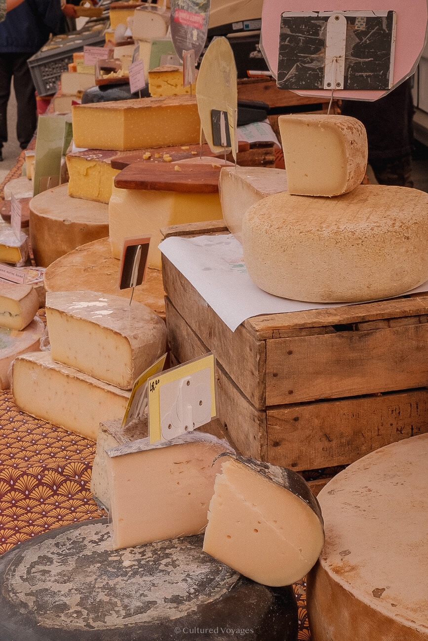 A display of various cuts and rolls of cheeses on wooden crates with labels to buy when visiting saint remy de Provence..