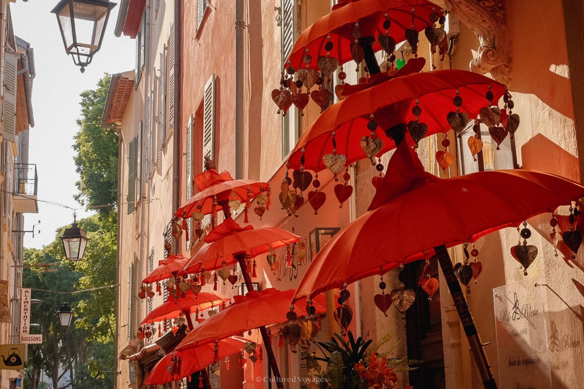 Red three-tiered umbrellas hanged beside a line of orange and warm colored buildings in Antibes