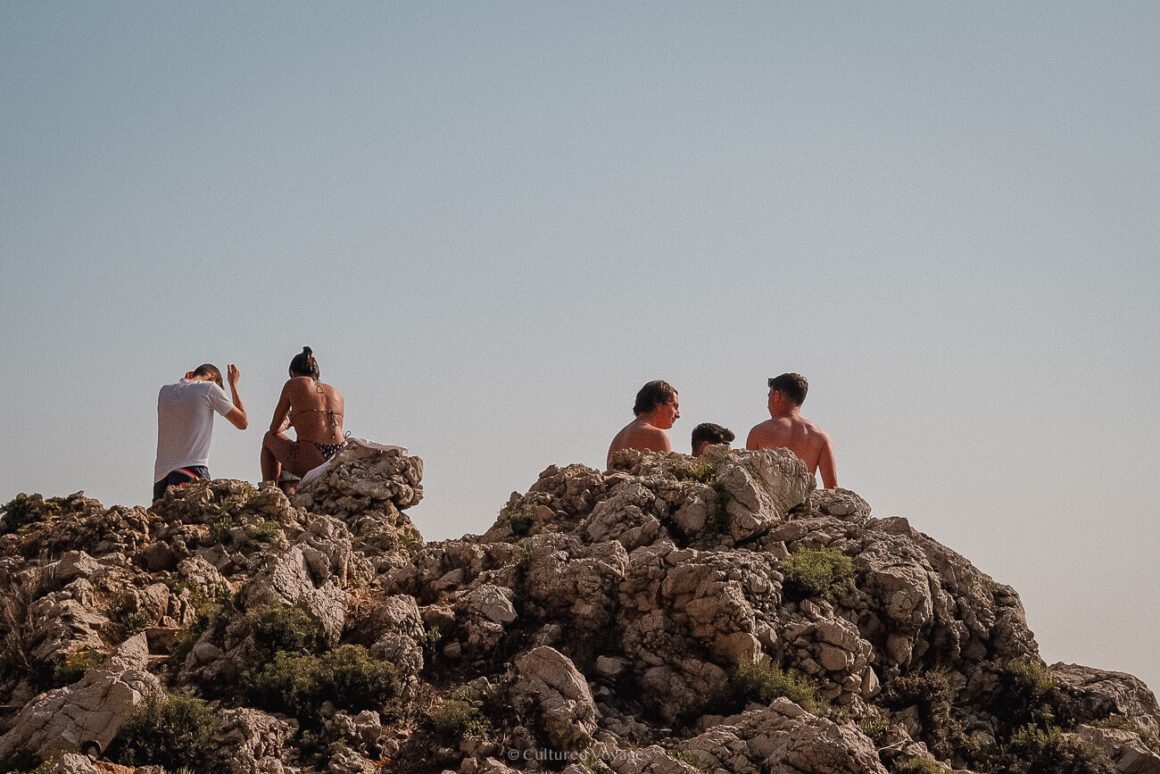 People sitting on a pile of rocks under sunny clear blue skies. This makes it worth visiting Antibes.