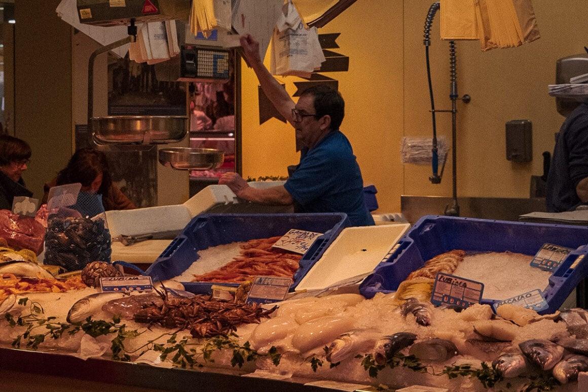 A fish market selling different kinds of seafood items with people buying and a person behind the counter in one of the best food markets in Seville Spain