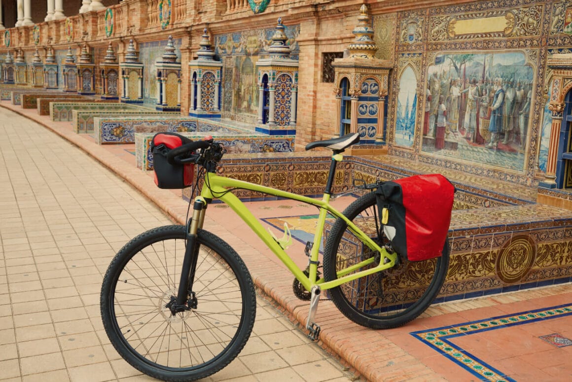 A green bike used during Seville bike tours parked in front of a wall filled with colorful frescoes and small pillars decorated with bright and detailed tiles