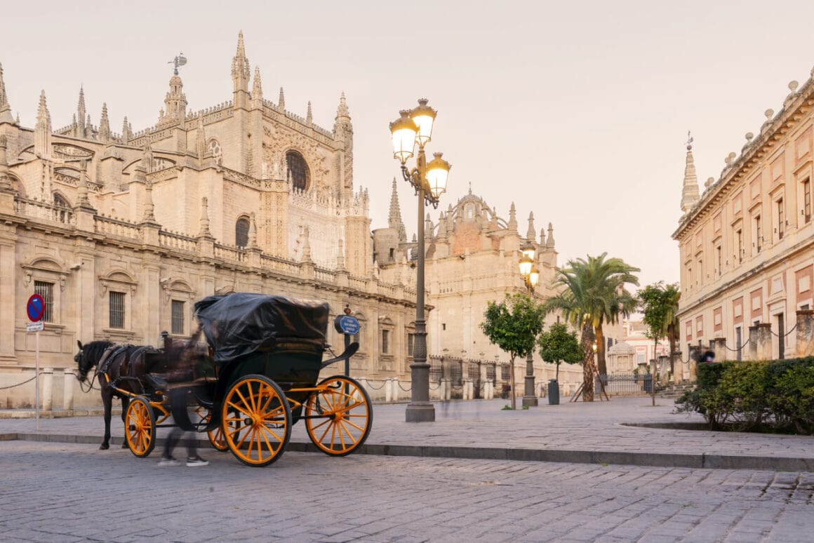 A carriage parked on a cobbled stone street, ideal for Seville bike tours, with the background of the white buildings filled with spires of the Seville Cathedral