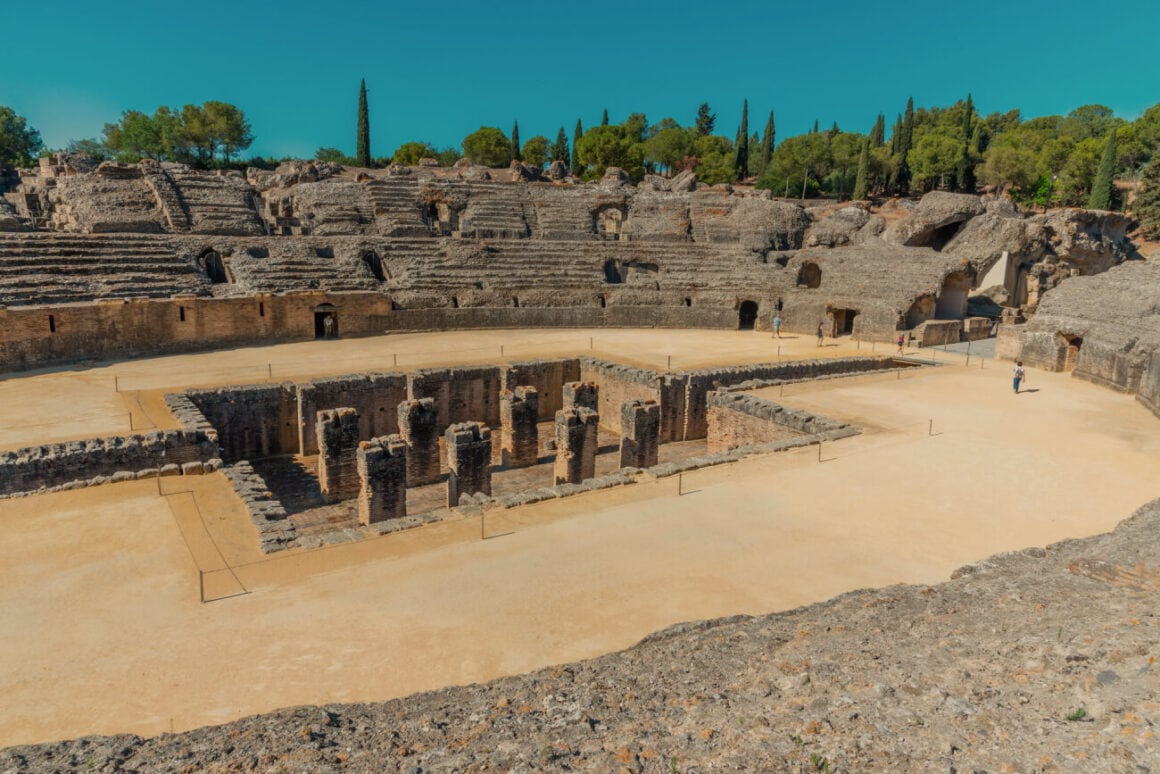 The ruins of the Amphitheatre of Italica with people walking under clear blue skies as a stopover during Seville bike tours