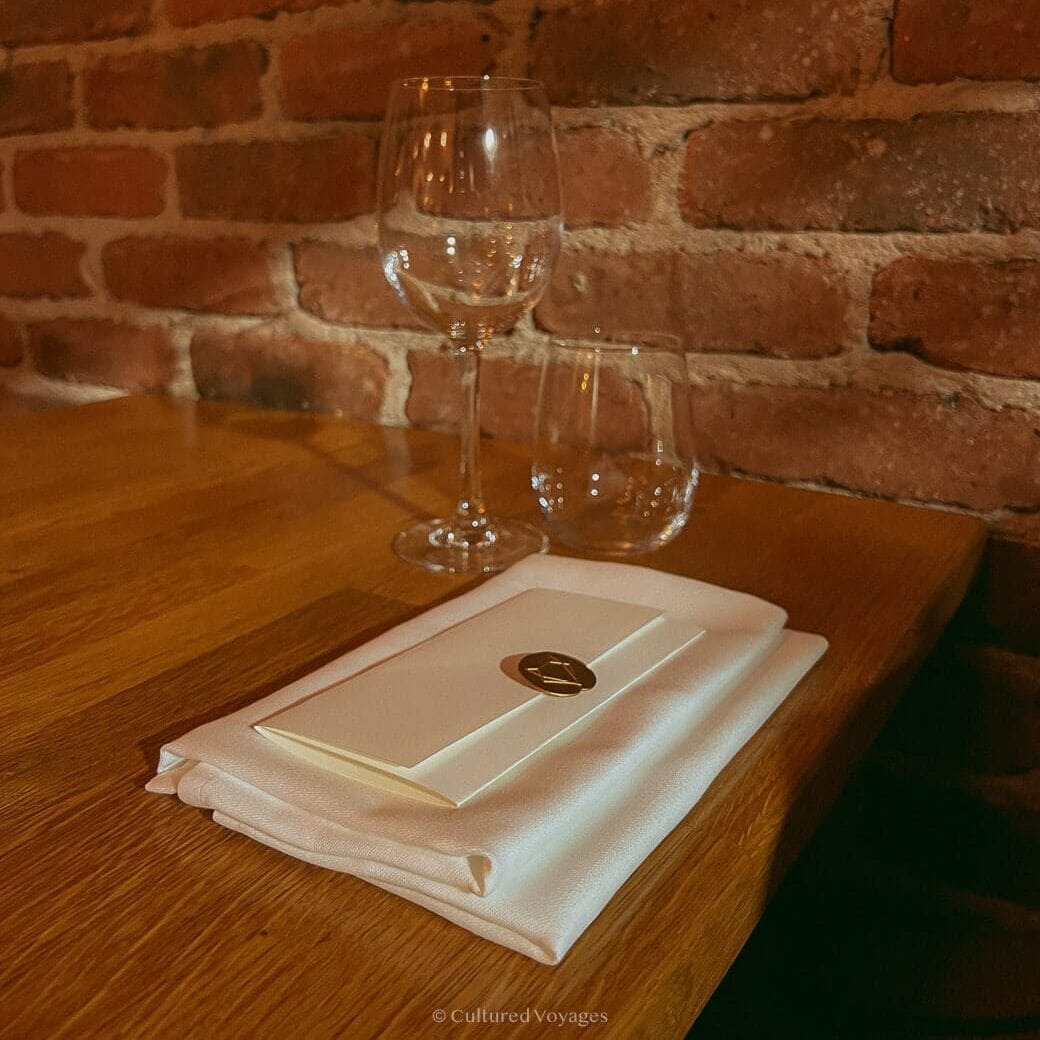 A wooden table with folded napkin and a folded piece of paper with empty glasses for wine and water during a worthy visit in Dublin's restaurants