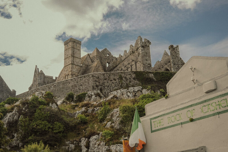 The Rock of Cashel rises above a stone wall and whitewashed building beneath a cloudy sky