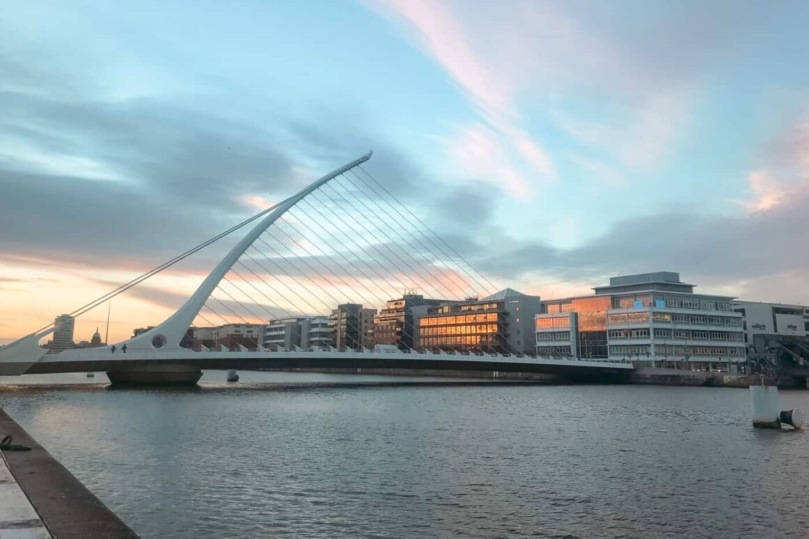 Samuel Beckett Bridge spanning the River Liffey with modern Dublin buildings beneath a pastel evening sky.