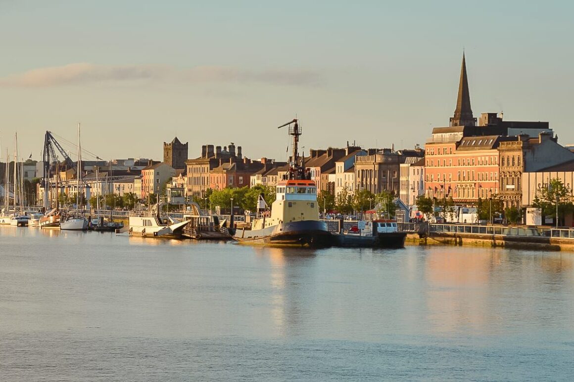 Waterford waterfront with boats, colourful historic buildings and a church spire beside the River Suir.
