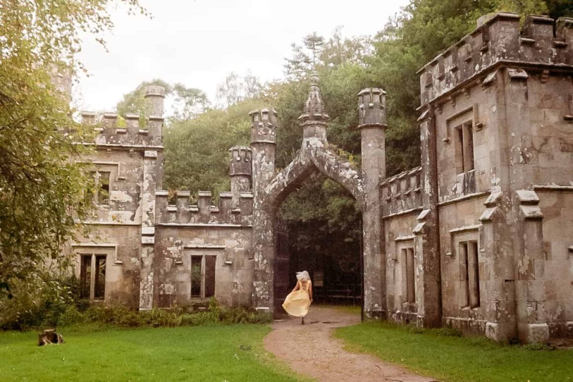 Weathered stone buildings with Gothic arches and castellated towers surrounded by woodland in Ireland.