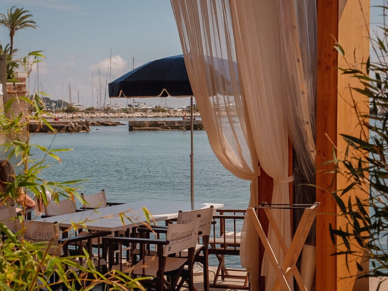 A shaded terrace overlooking blue water and moored boats on the French Riviera.