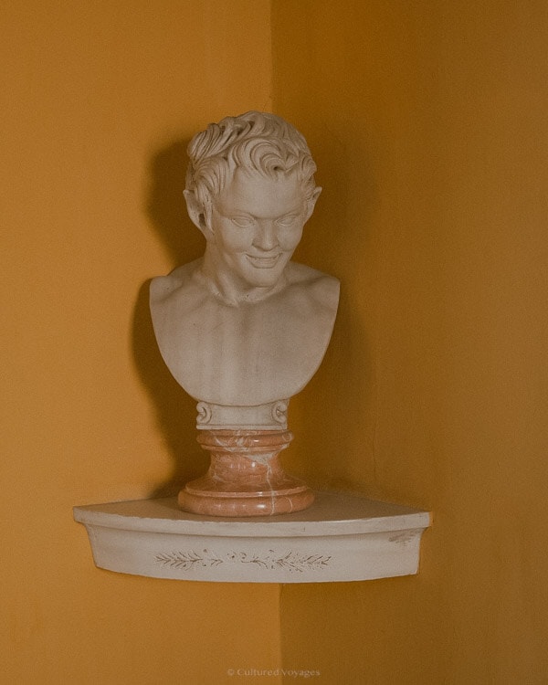 A marble bust of a man with pointy ears on a corner shelf against yellow walls. Curious about how many days in Seville? Explore the rich history and artistic wonders awaiting you.
