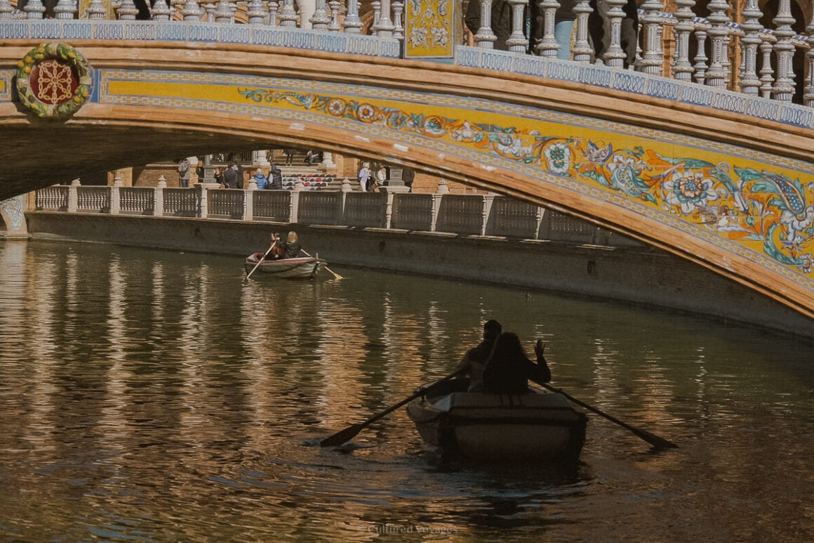 Boats rowing on crystal waters under a yellow bridge with painted flowers.